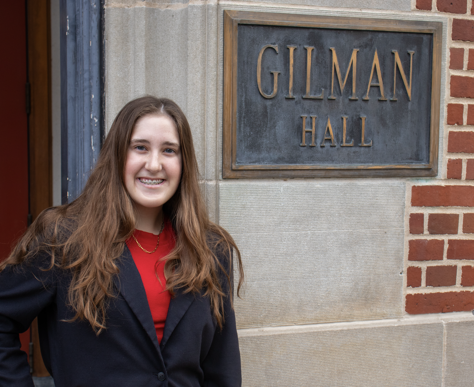 Emma Foley, chemistry student, smiling in front of Gilman Hall entrance plaque